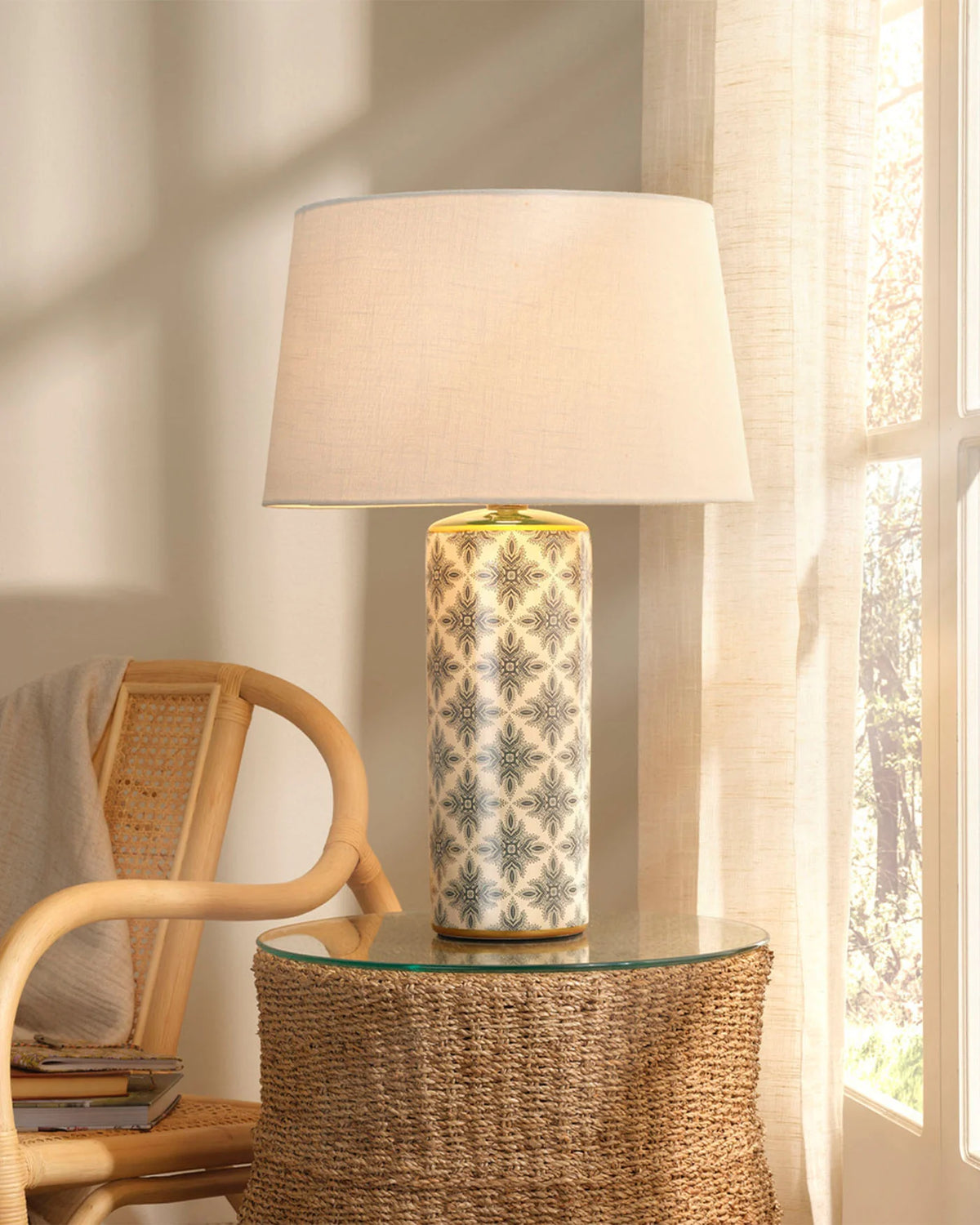 Decorative table lamp with a floral pattern on a glass table next to a wicker chair.
