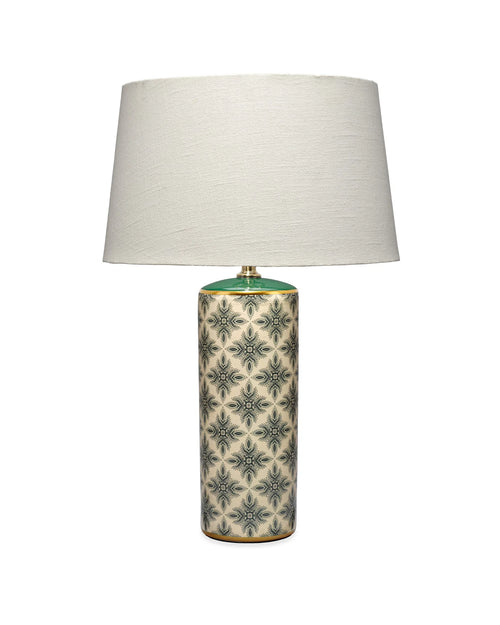 A table lamp with a large off-white fabric drum shade and a cylindrical ceramic base featuring a green and beige geometric pattern, set against a plain white background.