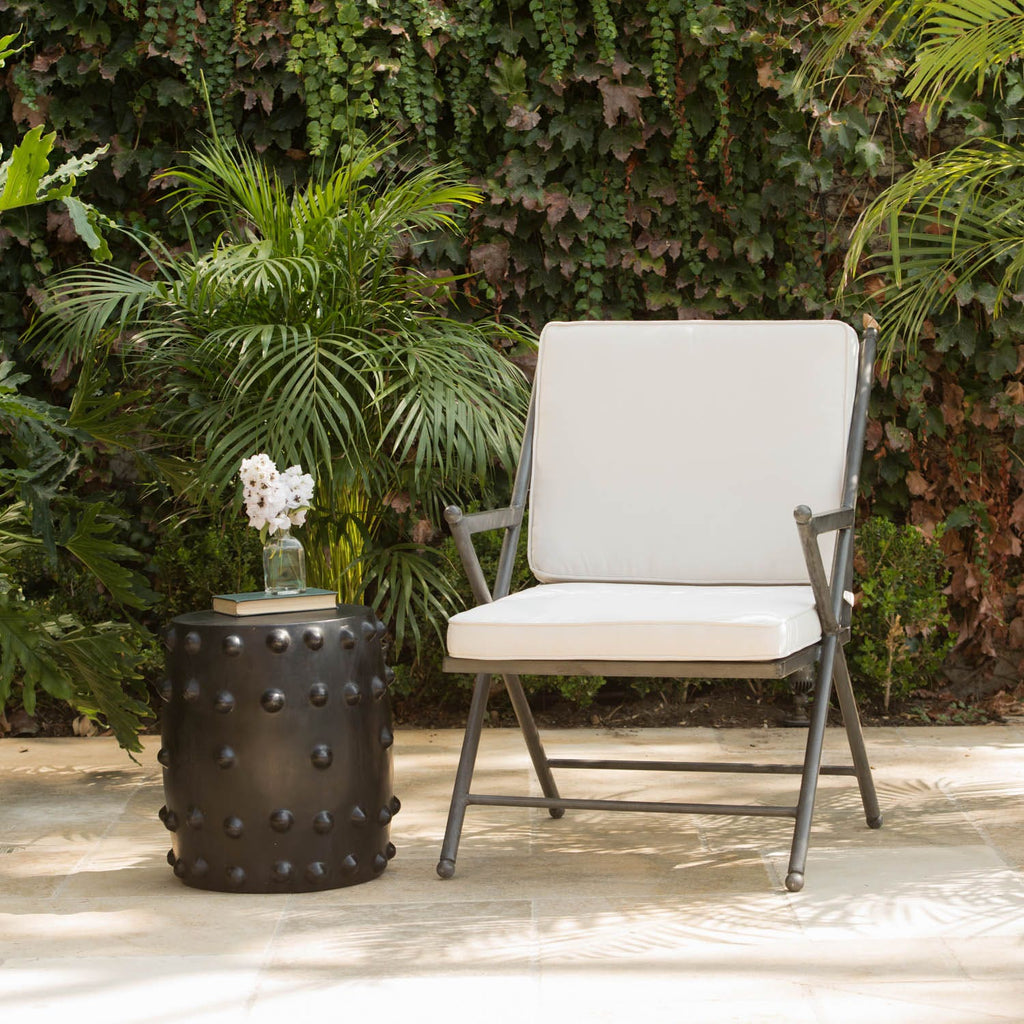 A black cylindrical garden stool with a matte finish and raised circular studs around the sides, styled in a luxury backyard setting.