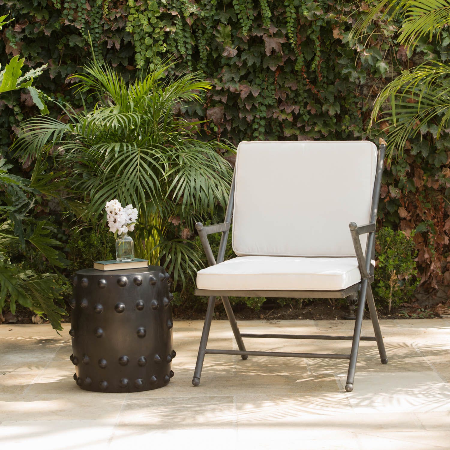 A black cylindrical garden stool with a matte finish and raised circular studs around the sides, styled in a luxury backyard setting.
