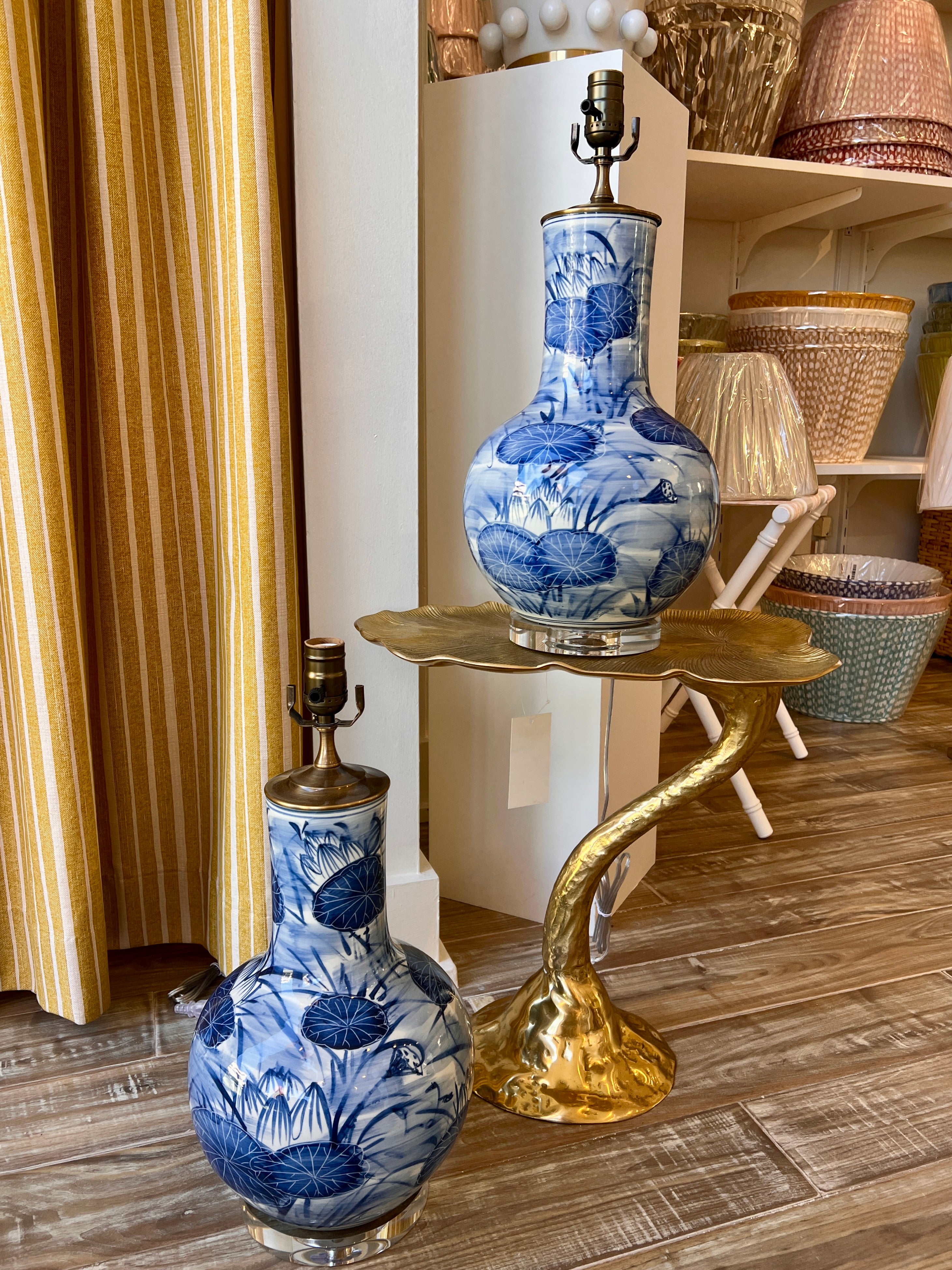 Two blue and white porcelain landscape vases with matching metal lamp bases, displayed on a gold swan-shaped side table in a home decor showroom.