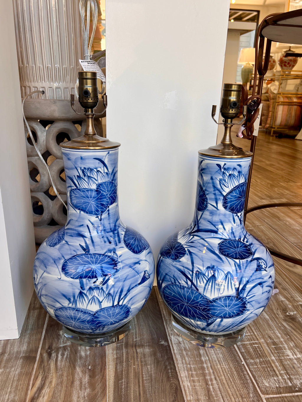 A pair of blue and white porcelain table lamps with lily pad pond designs, displayed on a wooden floor in a store setting.