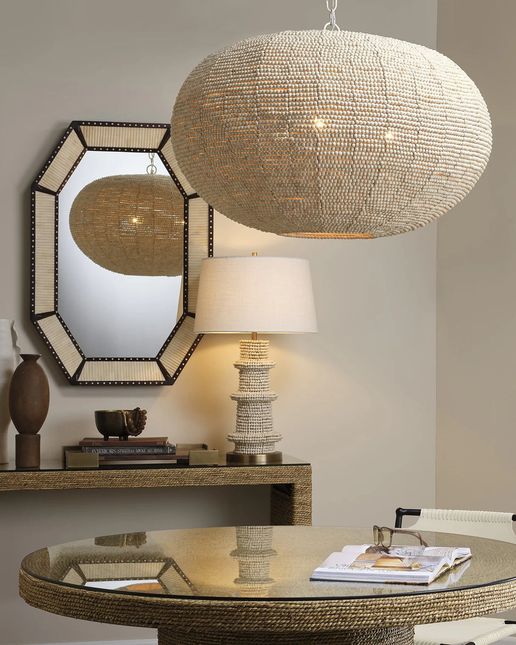 Artisanal table lamp made from hand carved mango beads with a dark brass base and white linen lampshade styled in a living room with naturally textured and hand-woven decor.