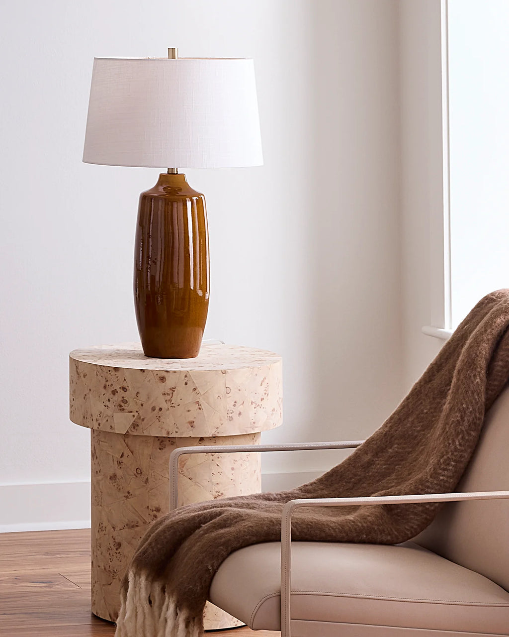 Table lamp with a rich toffee colored ceramic glaze and white linen lampshade styled on a natural wood side table