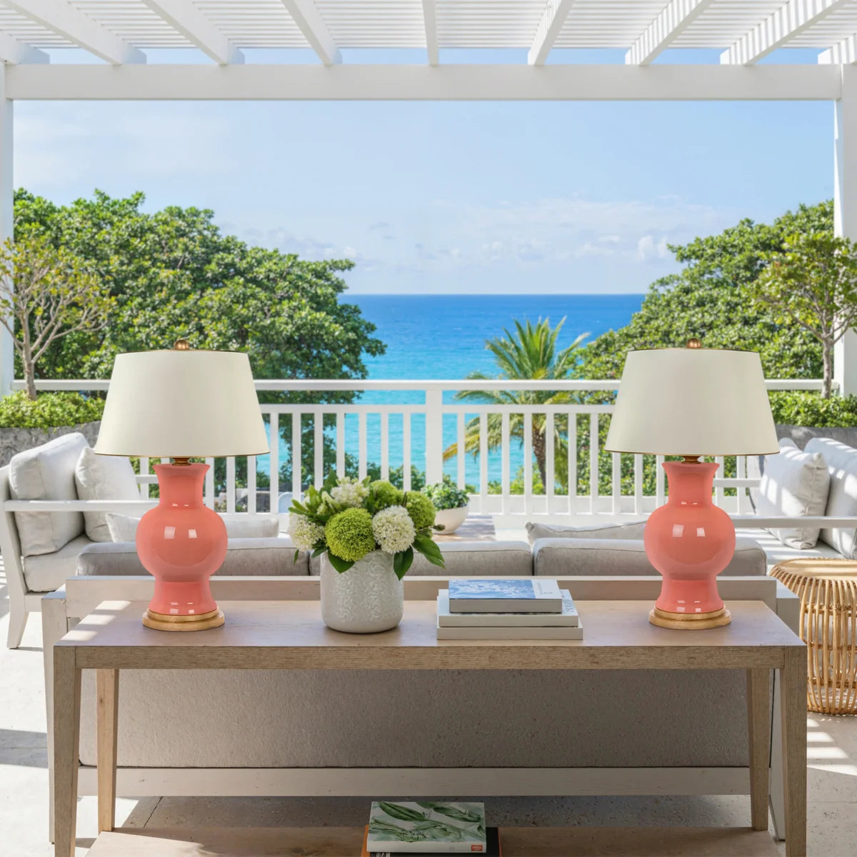 Coral ceramic table lamp with gold base and whtie lampshade with gold trim styled on an outdoor table