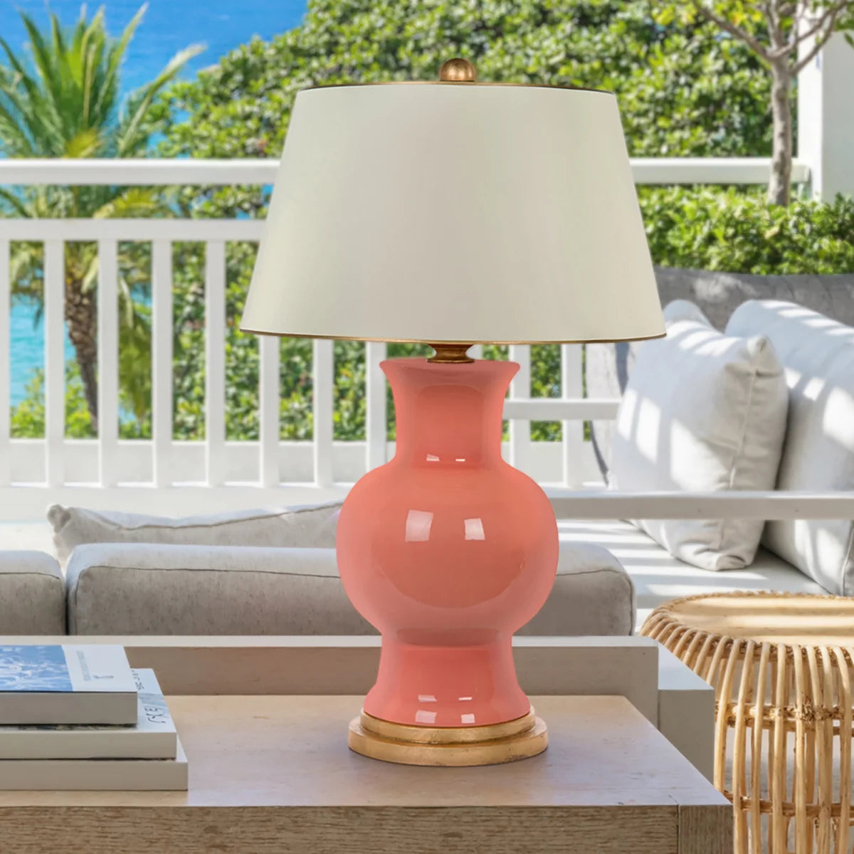 Coral ceramic table lamp with gold base and whtie lampshade with gold trim styled on an outdoor table