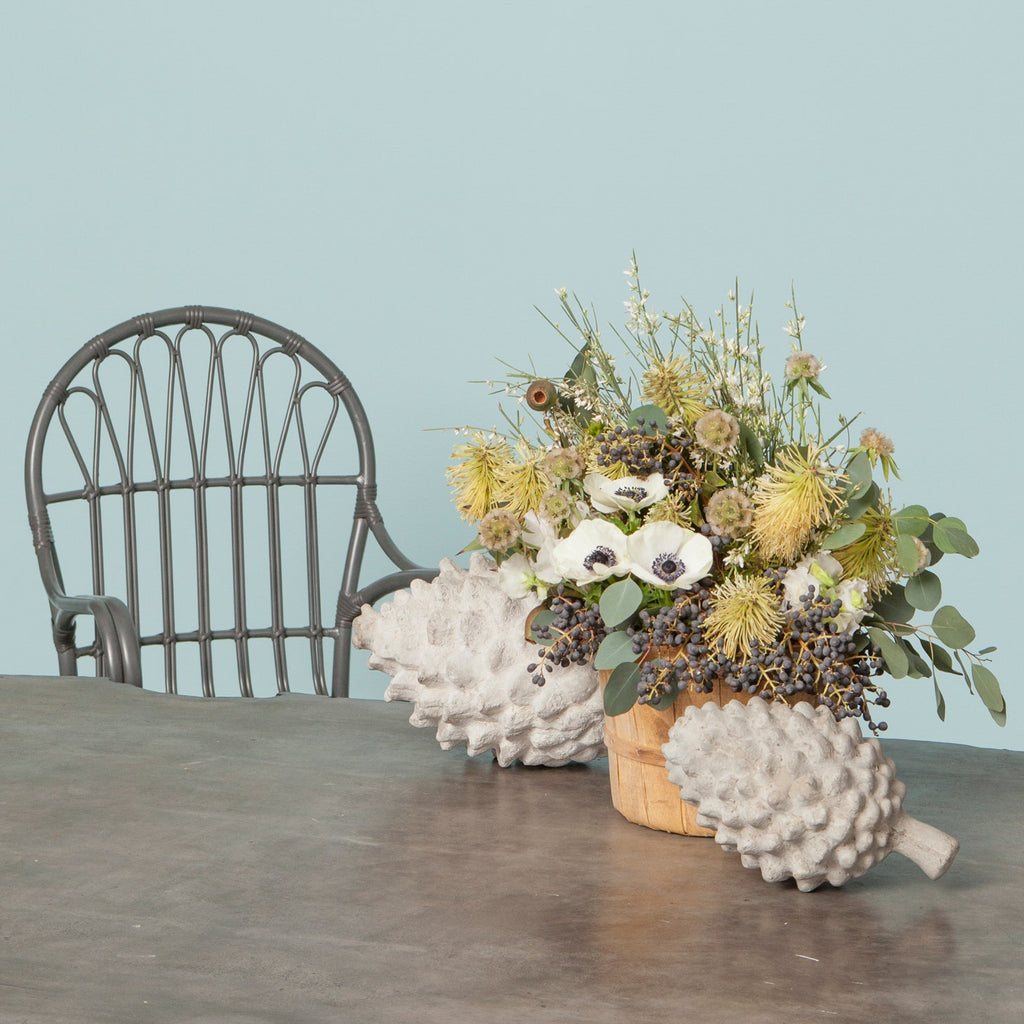 Decorative pinecone objects made from reconstituted stone in a light gray finish, styled on a table with flowers in Nashville, Tennessee