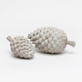 Decorative pinecone objects made from reconstituted stone in a light gray finish.