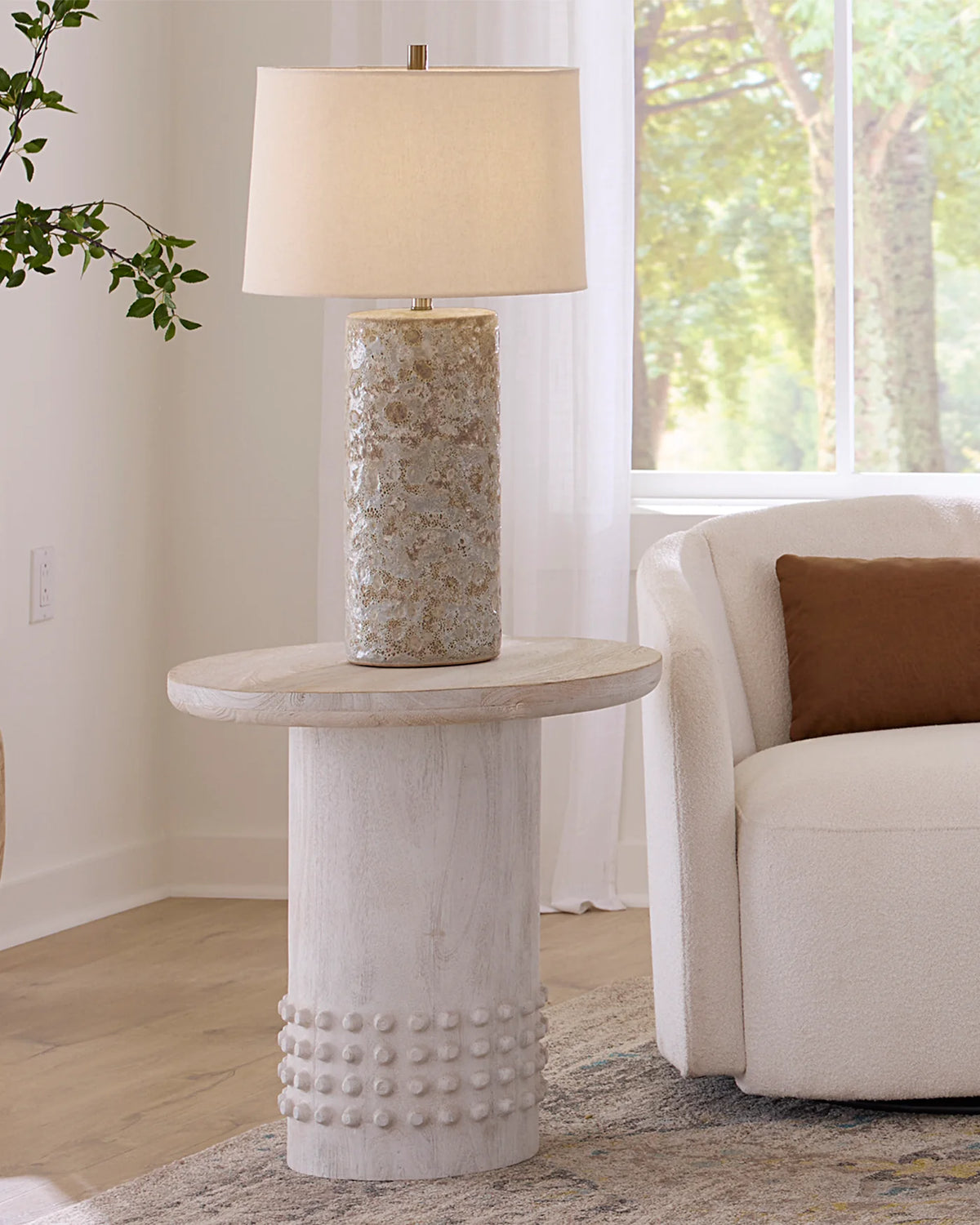 Decorative side table with textured base and lamp in a living room setting