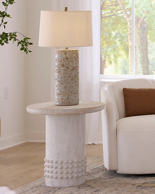Decorative side table with textured base and lamp in a living room setting