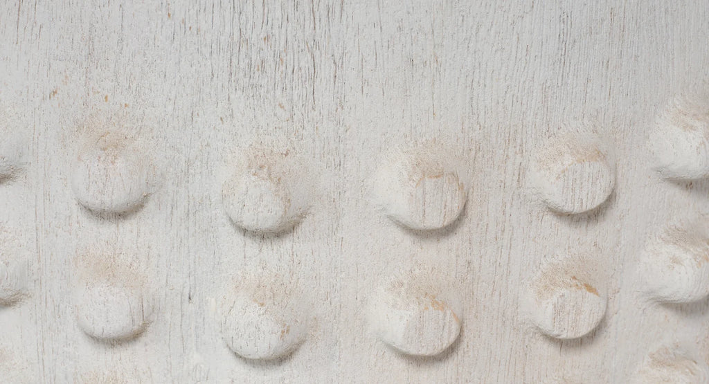 A close-up of a textured, off-white fabric or material surface with a repeating pattern of raised circular bumps.