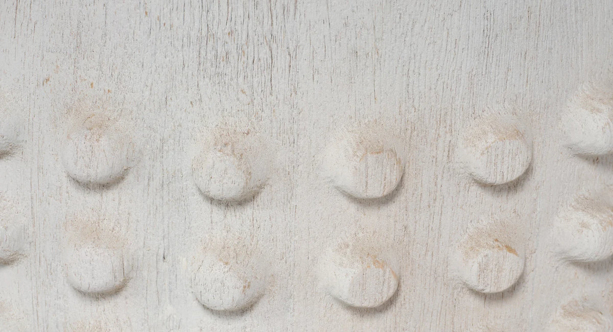 A close-up of a textured, off-white fabric or material surface with a repeating pattern of raised circular bumps.