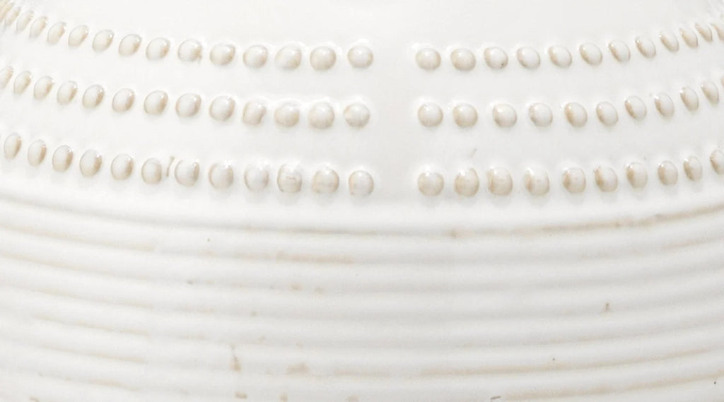 Close-up of a white ceramic vessel showing embossed rows of small raised dots and horizontal ridges.