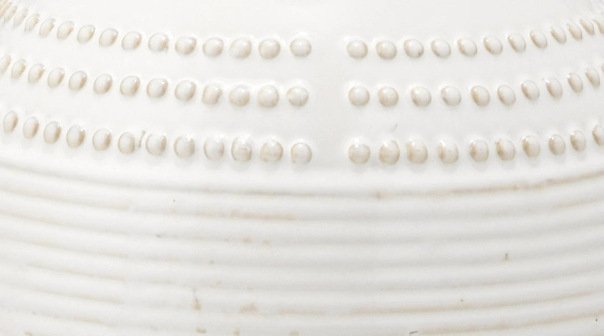 Close-up of a white ceramic vessel showing embossed rows of small raised dots and horizontal ridges.