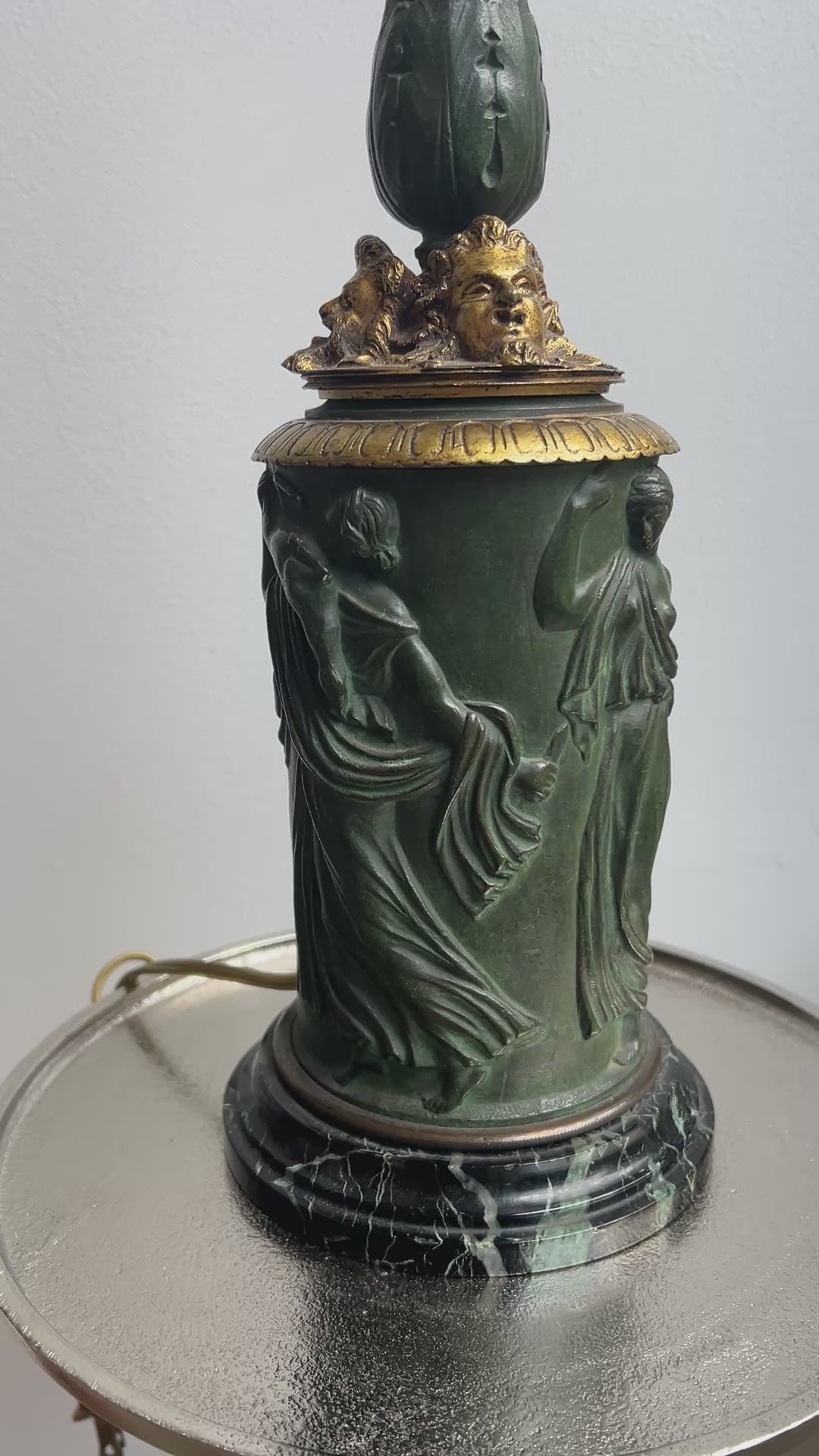An ornate antique Neoclassical Revival table lamp with a dark green carved column featuring classical female figures, a gold-gilt decorative collar, and a matching gold-toned spiral stem, with a black marbled base.