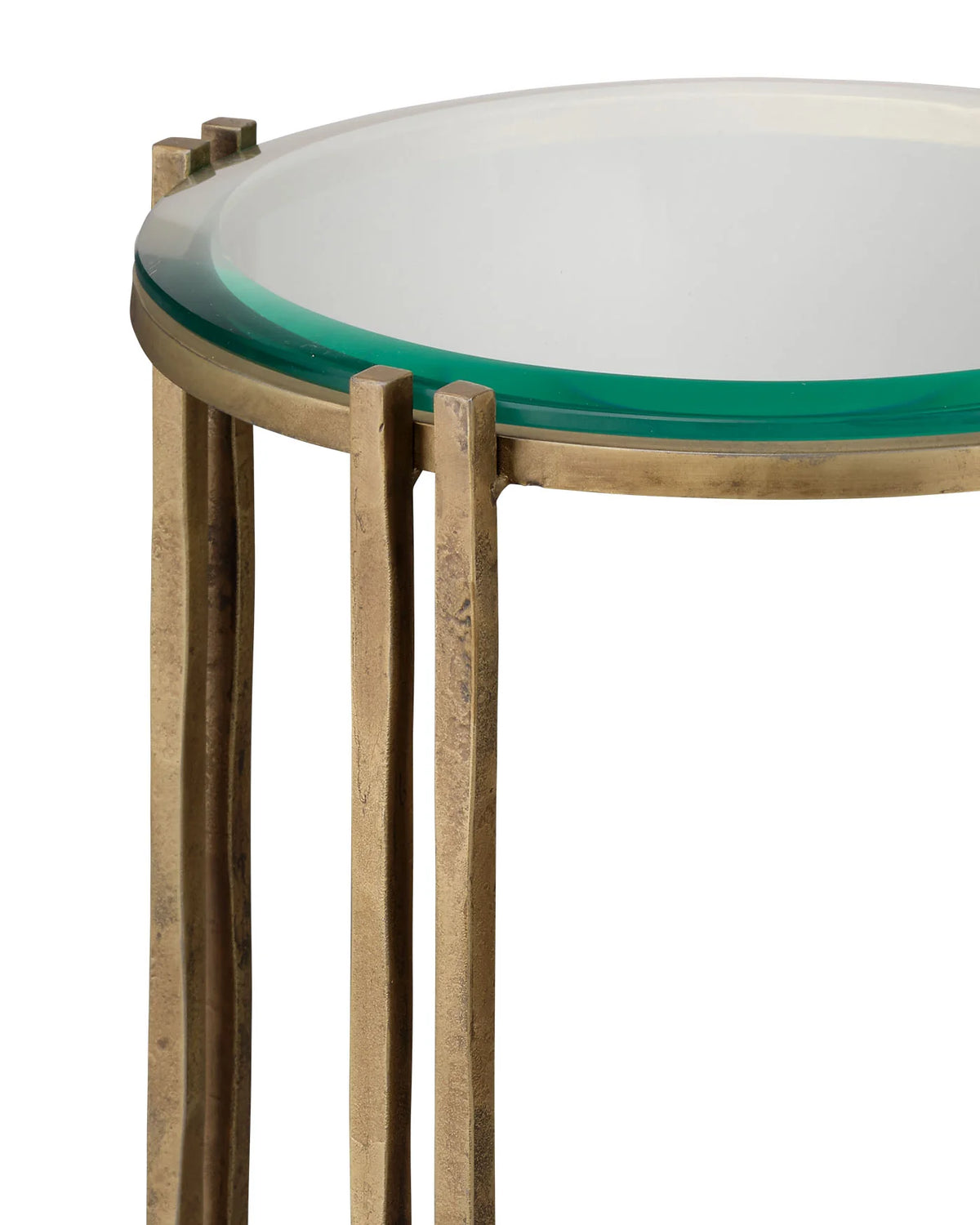 Close-up of a round side table with a clear glass top showing a green tint, supported by a distressed brass metal frame on a white background.