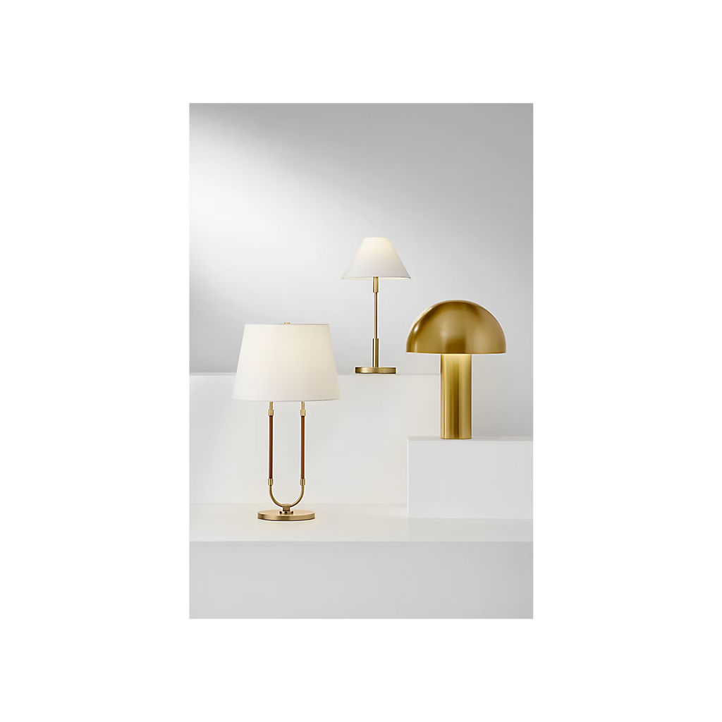 Katie Table Lamp by Lauren Ralph Lauren for Visual Comfort, featuring saddle leather-wrapped supports, warm brass accents, a circular brass base, and a white tapered lampshade.